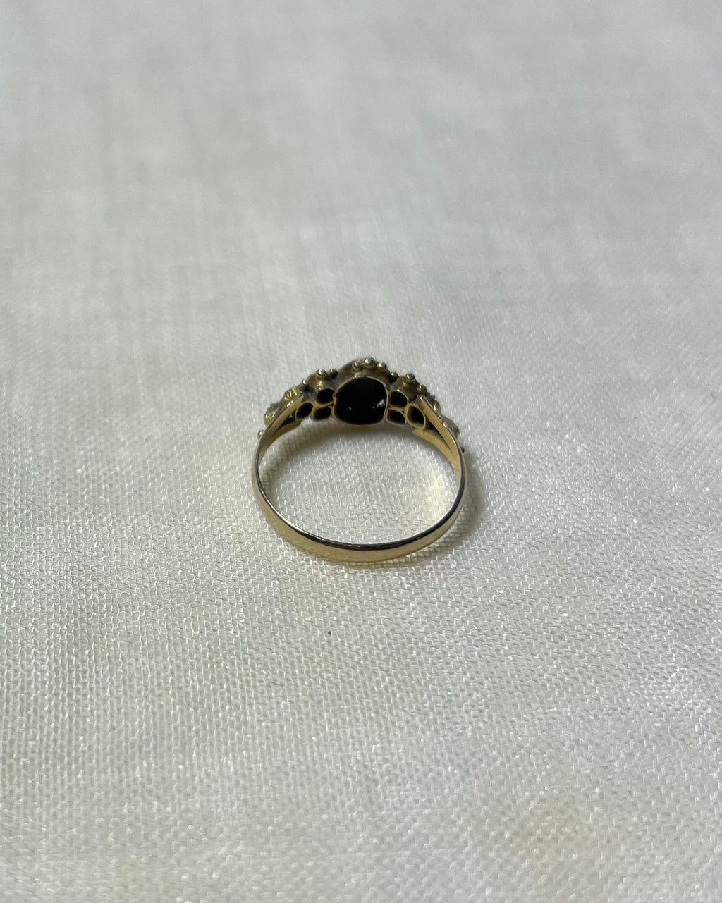 back view of gold stone set ring, resting on cream linen background