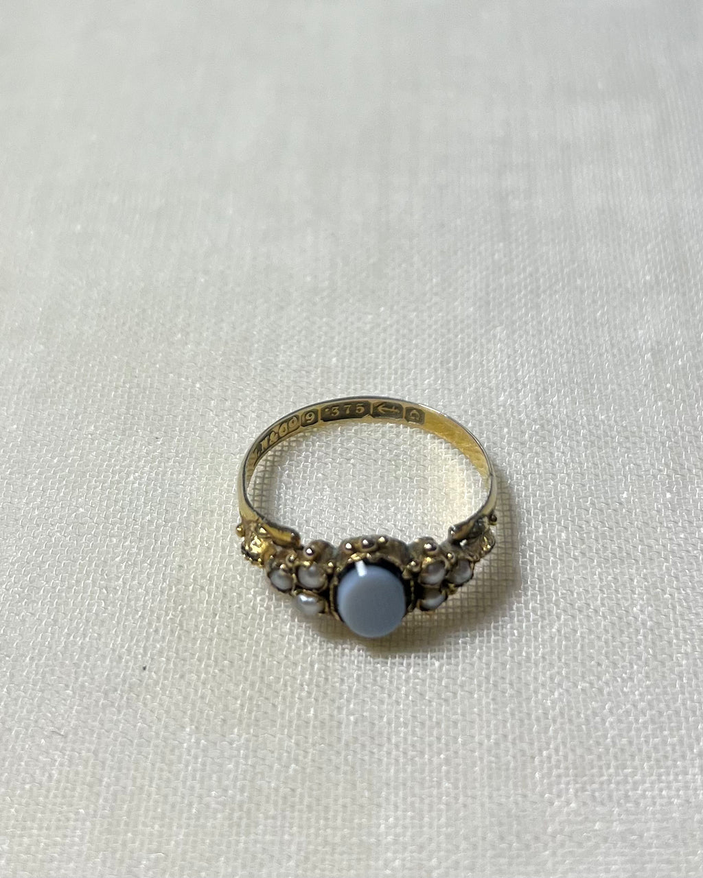 gold stone set ring with visible hallmark on the band, marked 375 with anchor symbol and letter G, resting on cream linen background