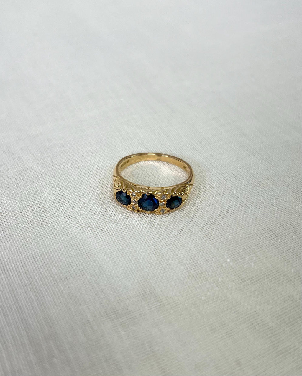 Gold ring with three blue stones on a light fabric background