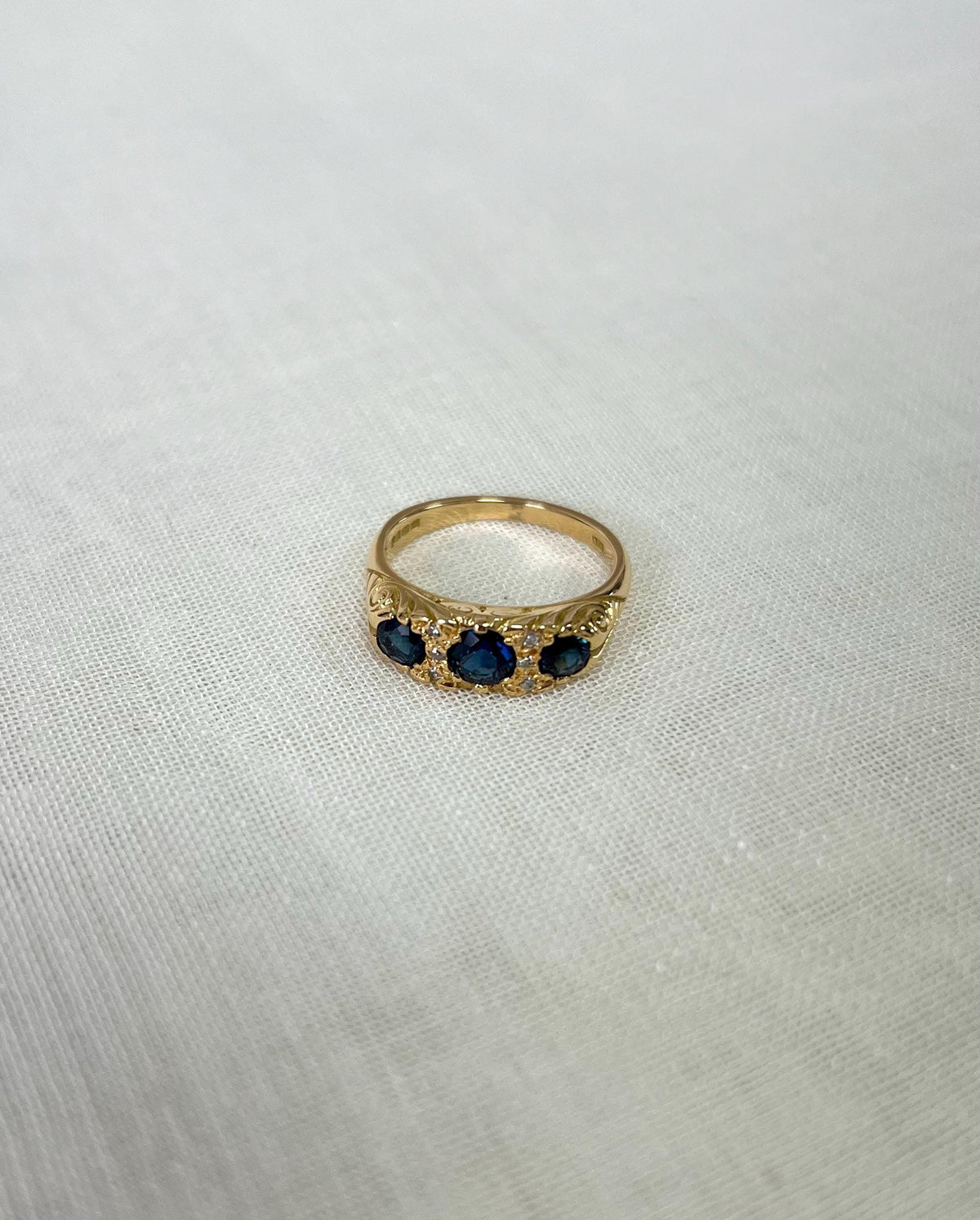 Gold ring with three blue stones on a light fabric background