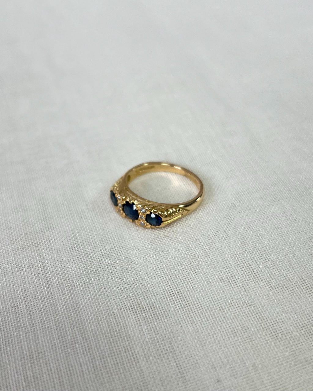 Gold ring with 3 blue stones on a white fabric background