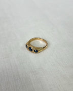 Gold ring with 3 blue stones on a white fabric background