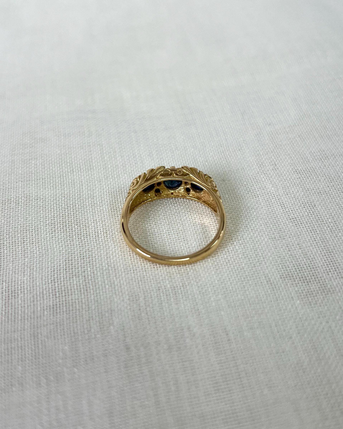 Gold ring with three blue gemstones on a white fabric background