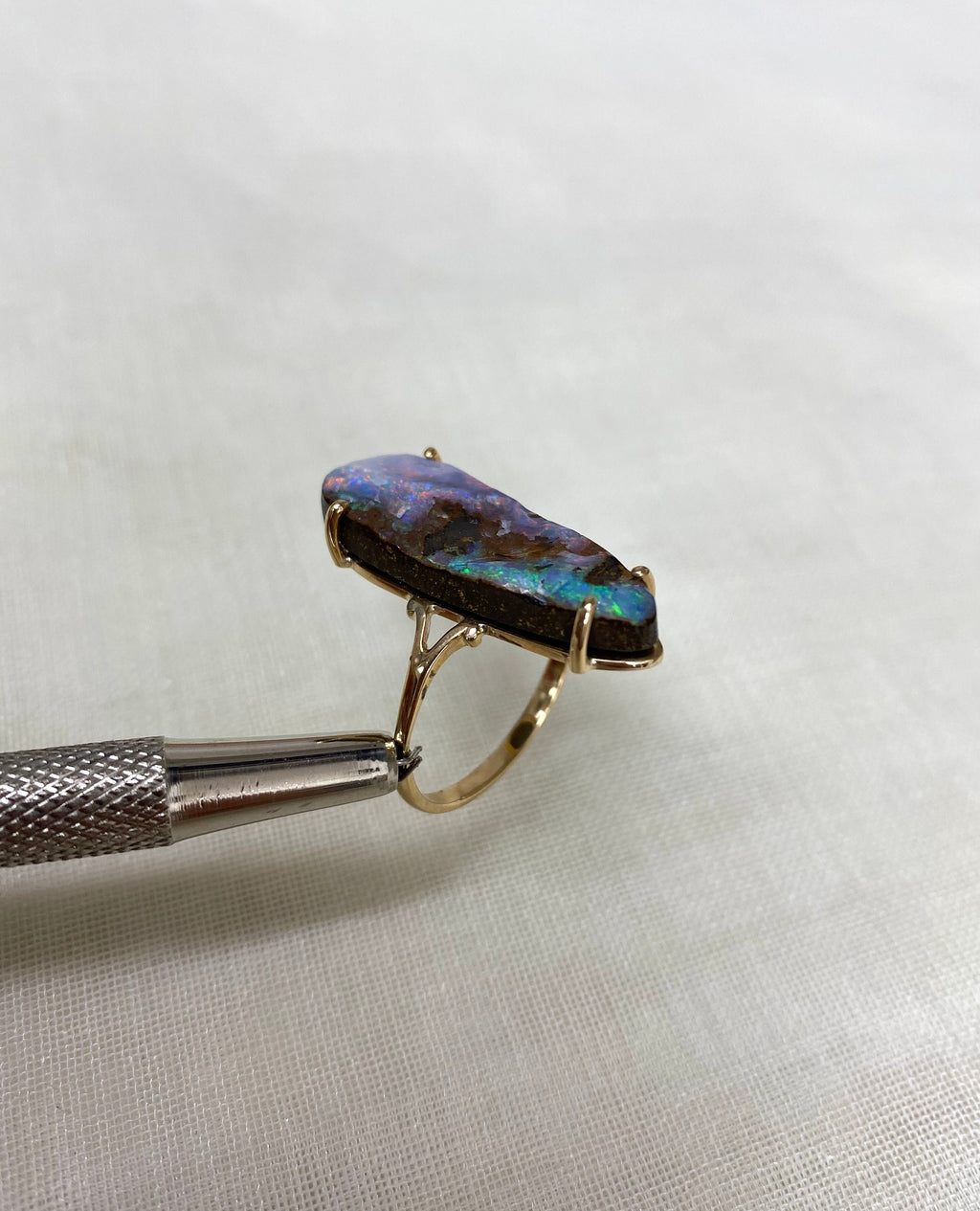 large opal gold ring held by tweezers against white background