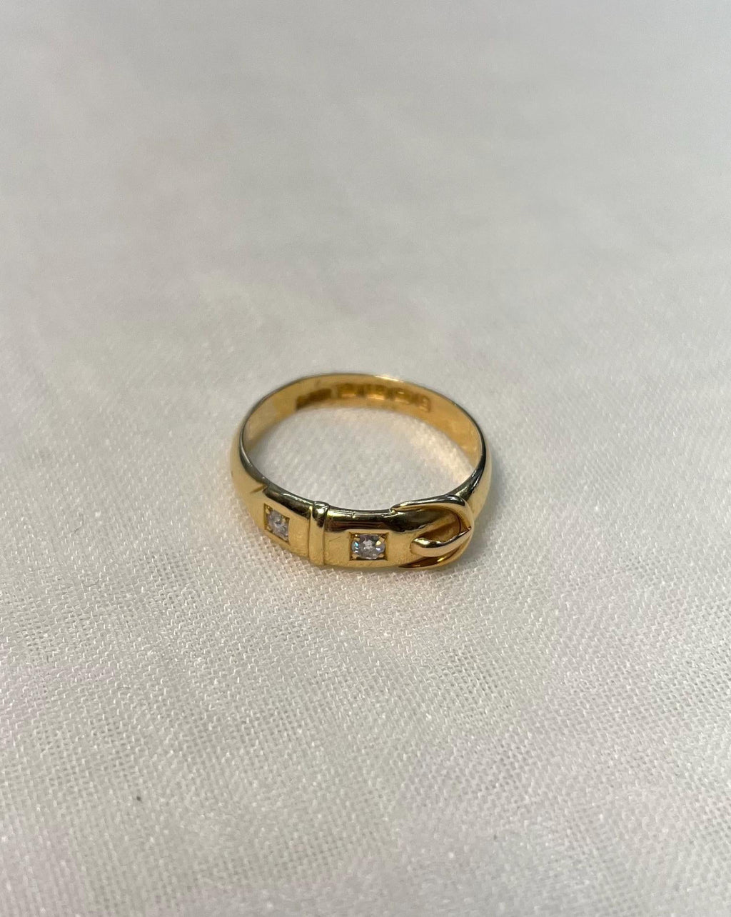 gold buckle ring with 2 diamonds, resting on white fabric background 