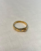 gold buckle ring with 2 diamonds, resting on white fabric background 
