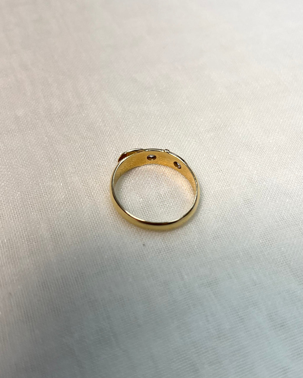 back view of gold band set with diamonds, resting on white fabric background 