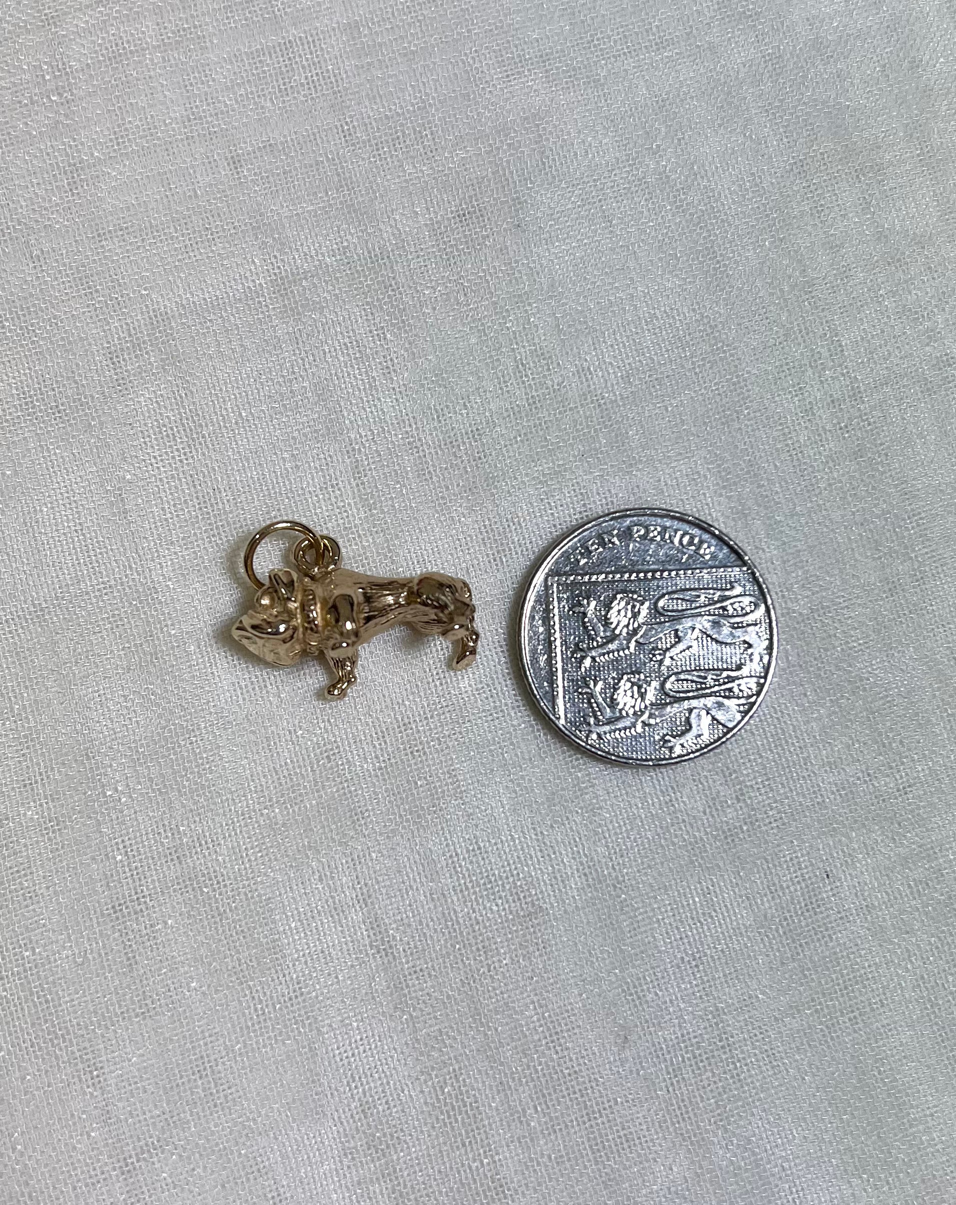 gold dog charm next to ten pence coin on white fabric background 