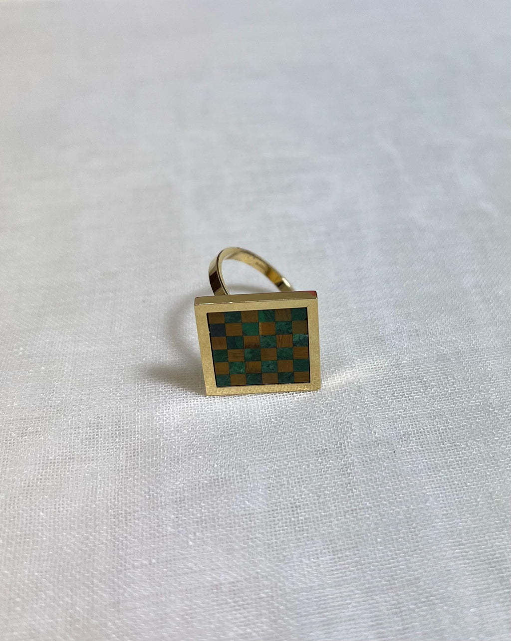 Gold ring with a green and brown checkered design on a white fabric background