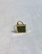 Gold ring with a green and brown checkered design on a white fabric background
