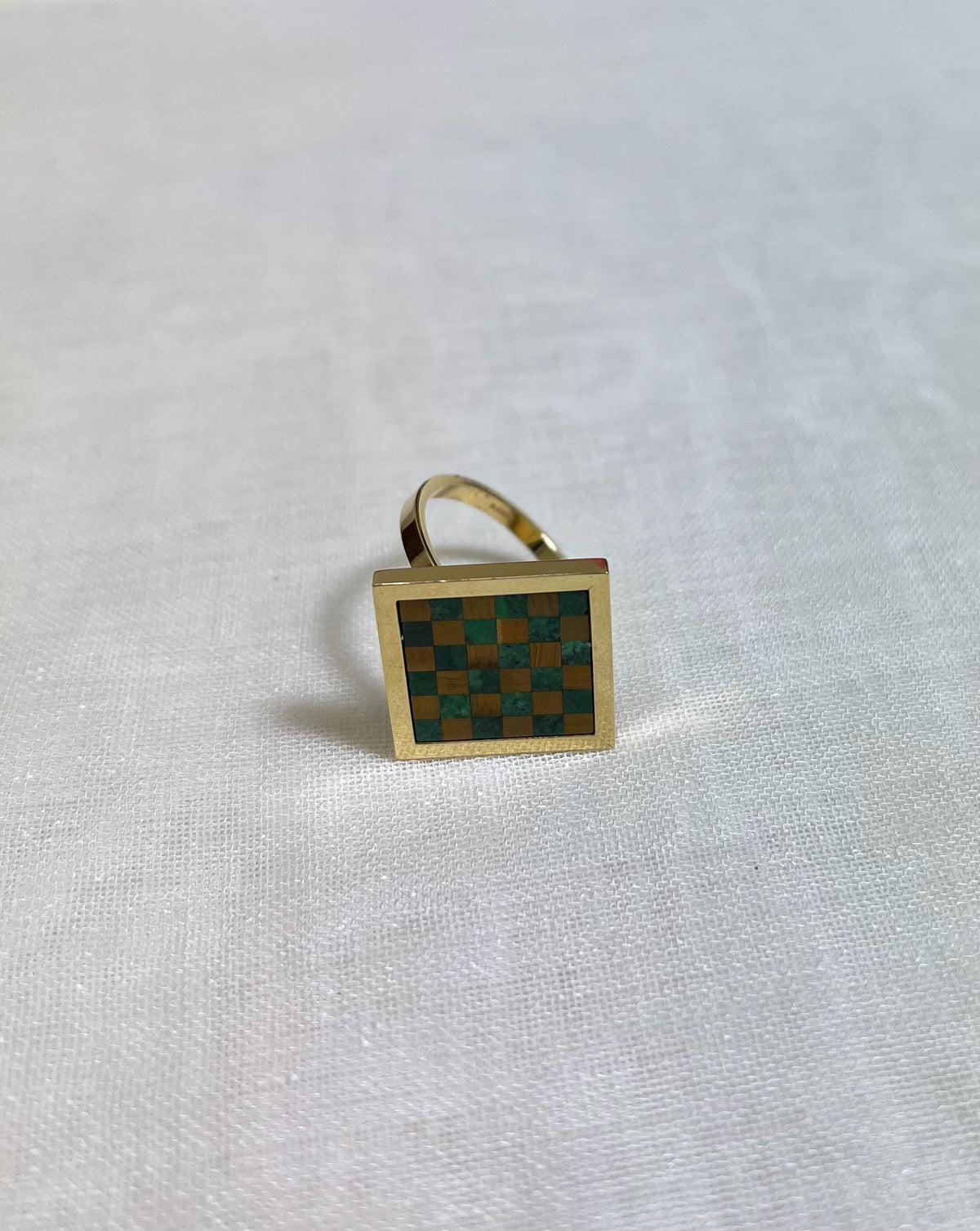 Gold ring with a green and brown checkered design on a white fabric background
