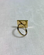 back view of gold square ring on white fabric background 
