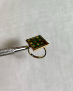 gold square ring with green and brown checkerboard design on white fabric background