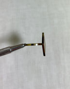 side view of gold square ring held by silver tool on white fabric background 