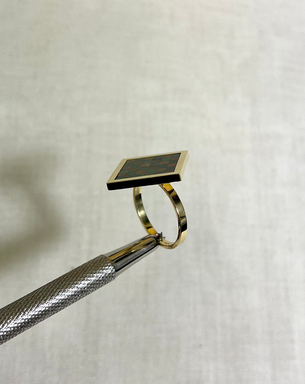 A gold square ring with checkerboard design on white fabric background 