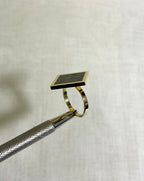 A gold square ring with checkerboard design on white fabric background 