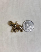gold elephant charm next to ten pence coin on white fabric background 