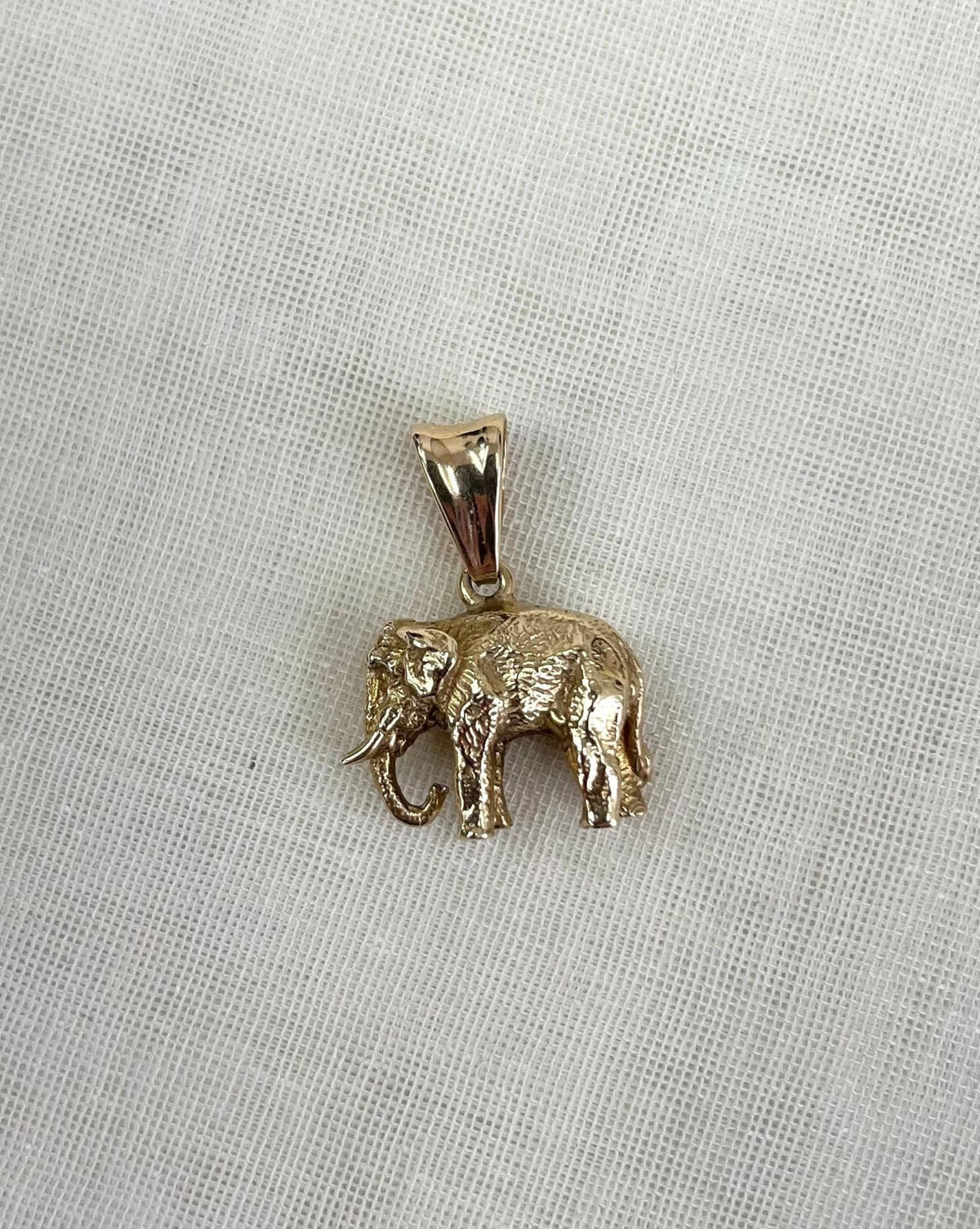 Gold elephant pendant on a cream fabric background
