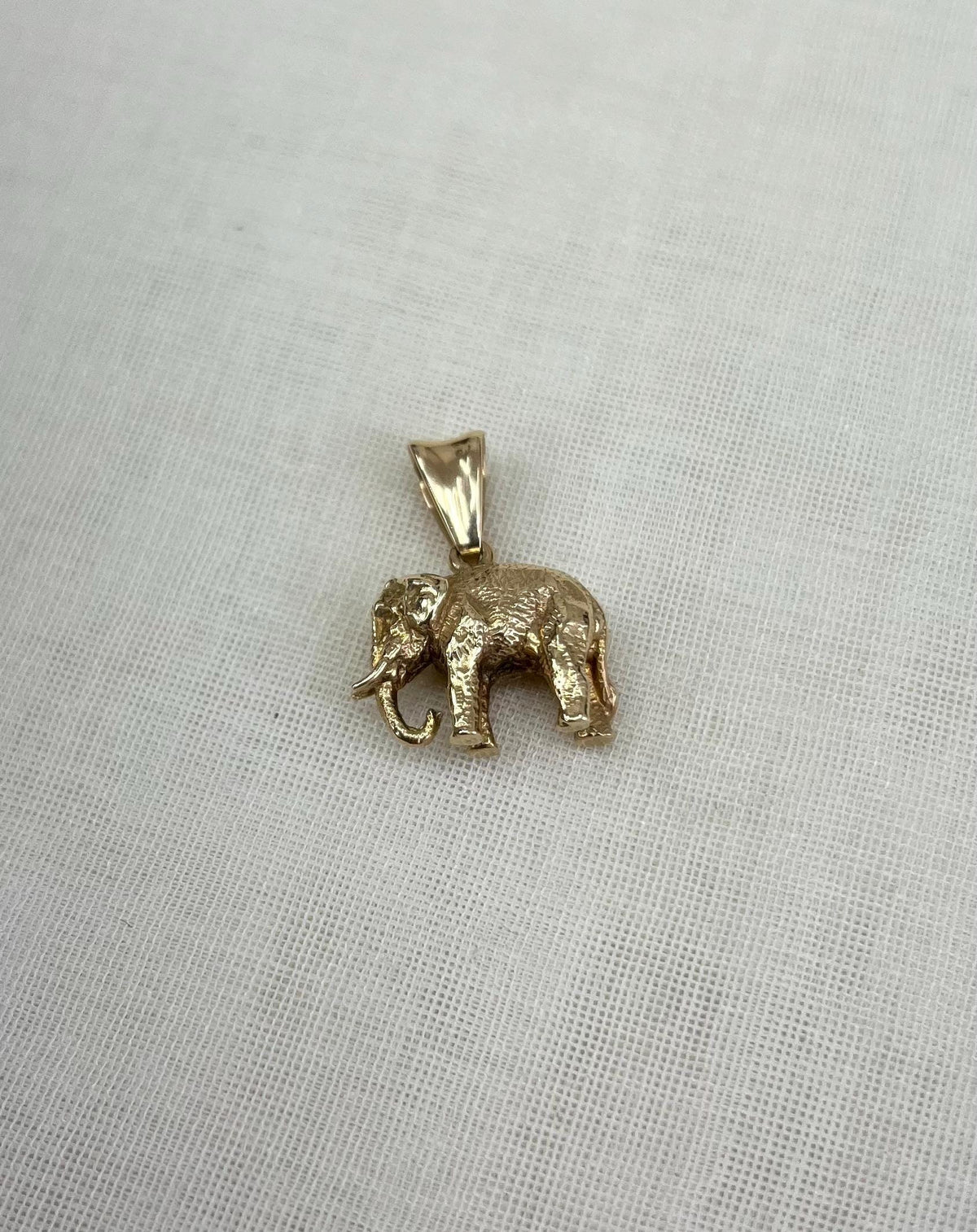 Gold elephant pendant on a light fabric background