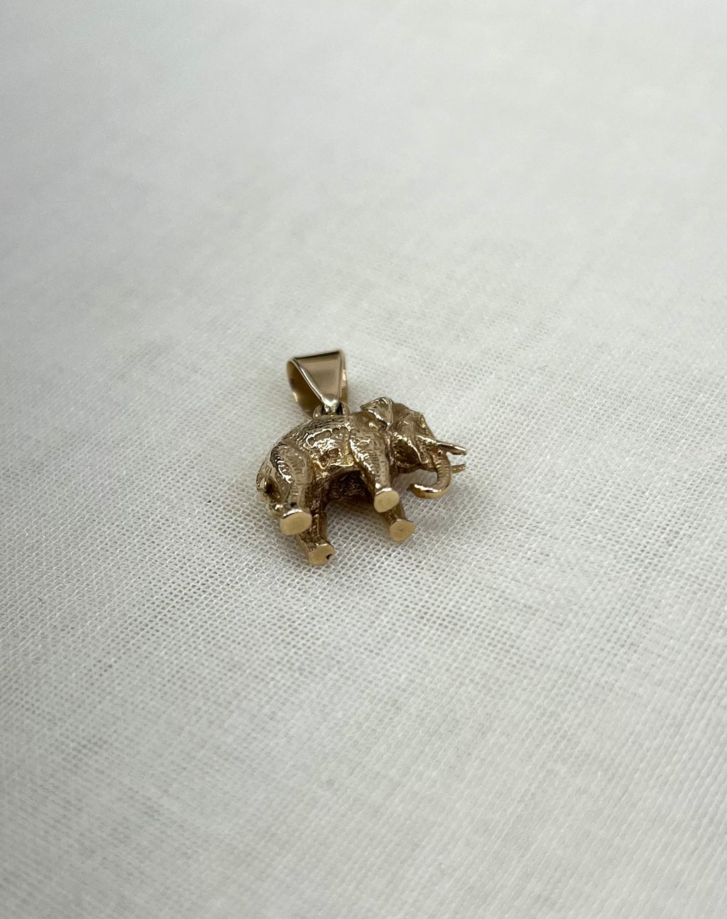a gold elephant pendant on cream fabric background