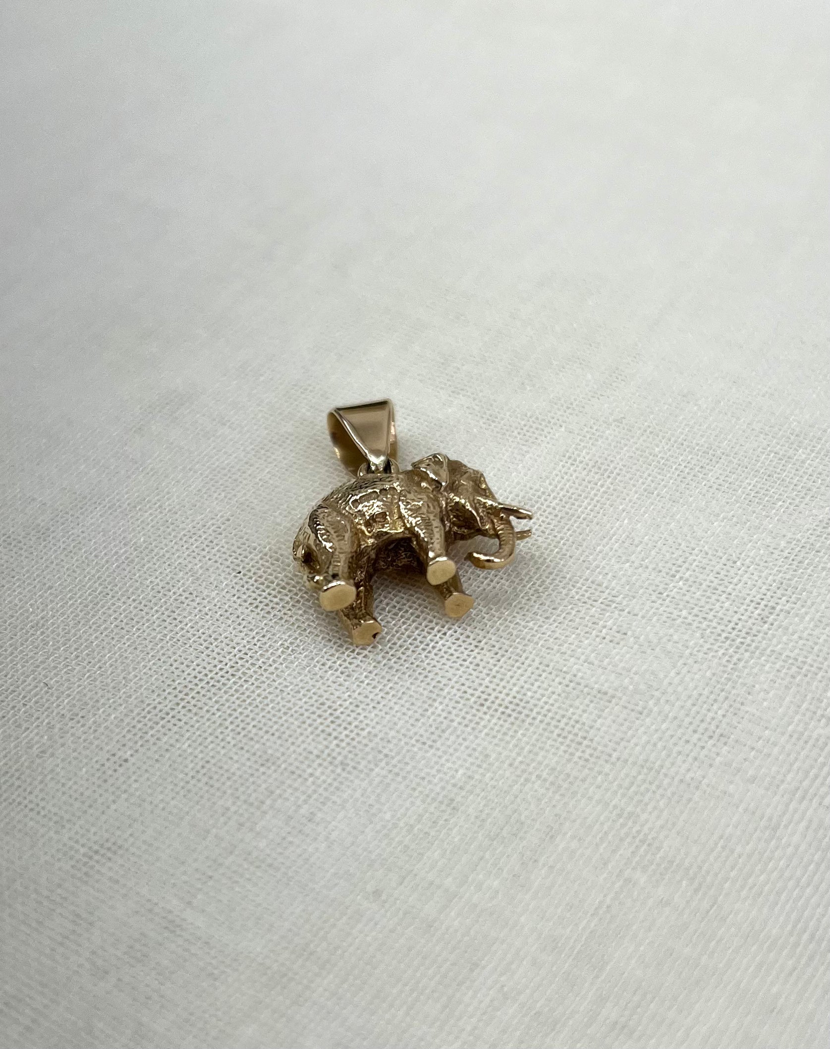 a gold elephant pendant on cream fabric background