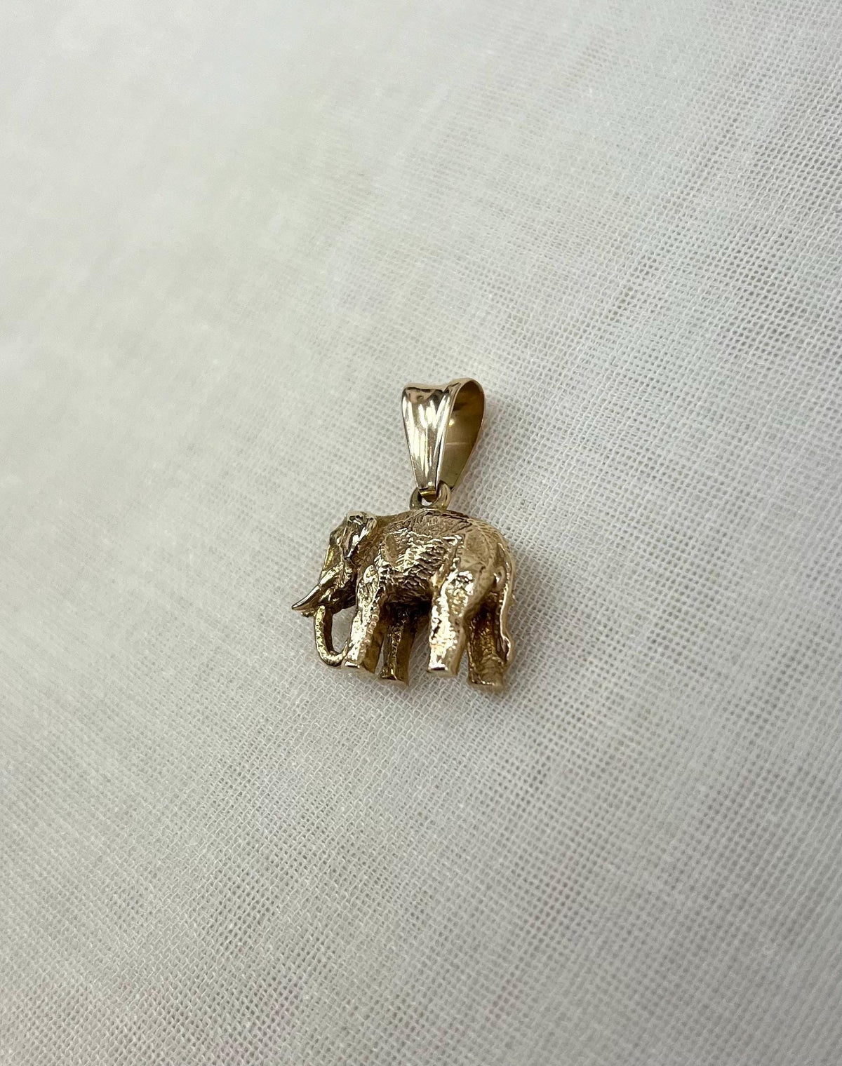 Gold elephant pendant on a light fabric background