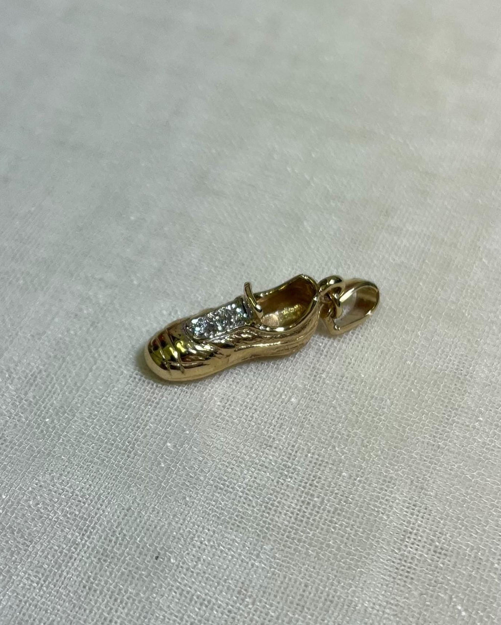 Gold shoe charm with embedded stones on a light fabric background