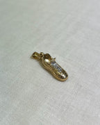 Gold shoe-shaped pendant with embedded stones on a white fabric background