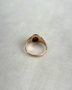 back view of gold ring with red gemstone on white fabric background