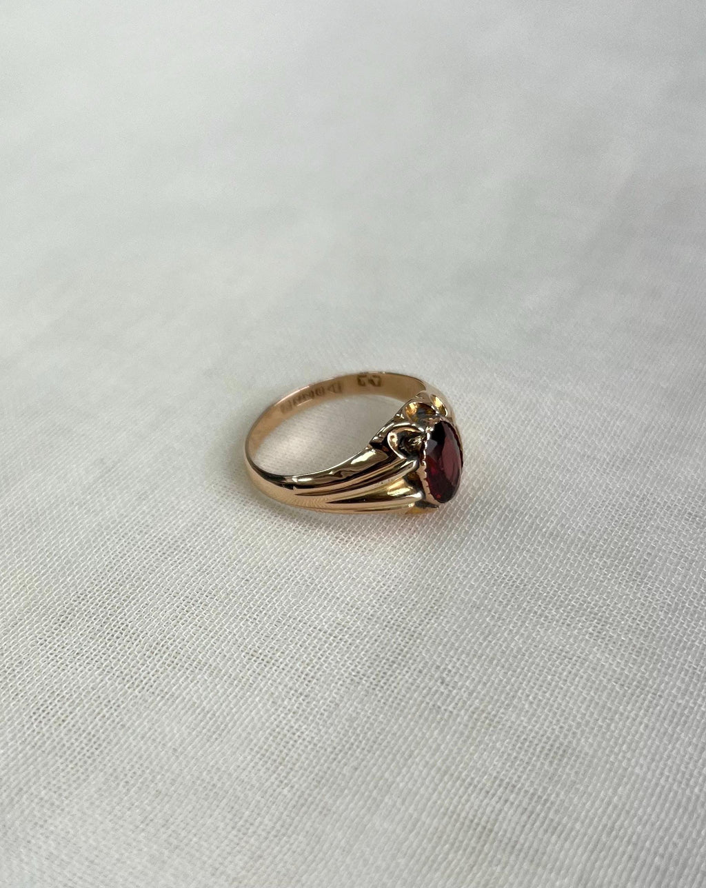 Gold ring with a red gemstone on a light gray background