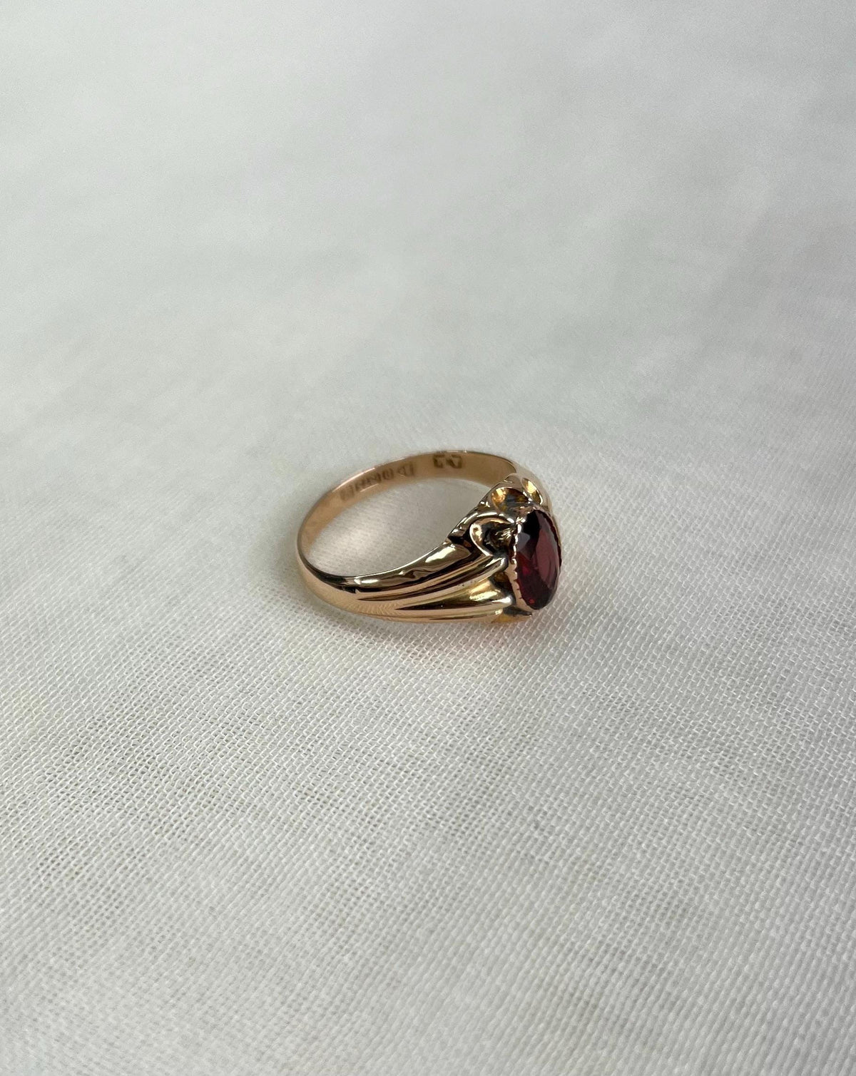 Gold ring with a red gemstone on a light gray background