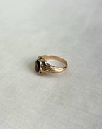 Gold ring with a red gemstone on a light gray background