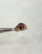 Gold ring with a red gemstone held by tweezers on a white background