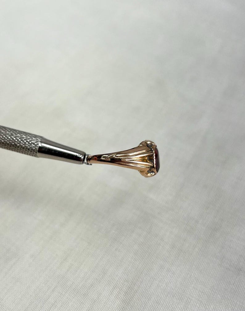 side view of gold ring held by silver metal tool above cream background 