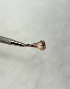 side view of gold ring held by silver metal tool above cream background 