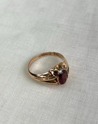 gold ring with red gemstone and visible hallmark in focus, resting on textured off white background