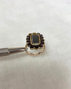 side view of garnet gold ring held by silver tools above white fabric background 