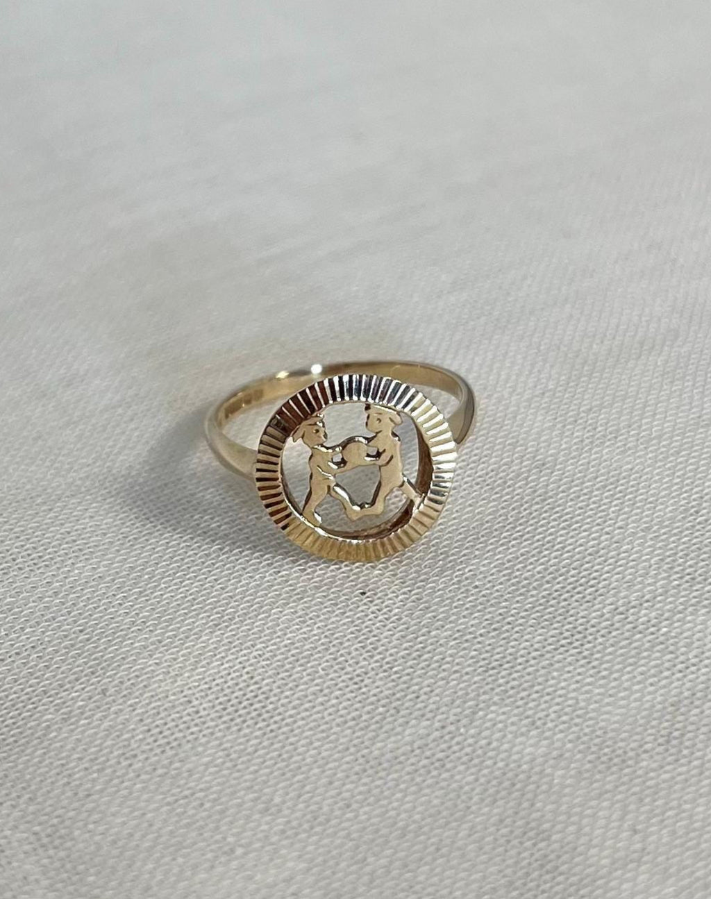 gold gemini openwork circular ring on light fabric background 