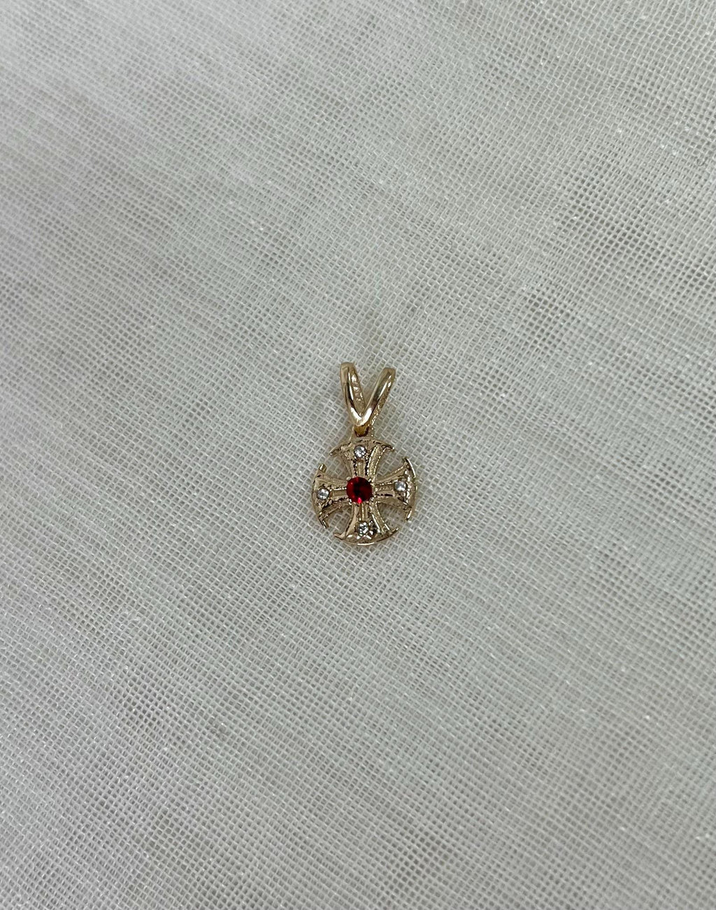 gold canterbury cross pendant resting on beige fabric background