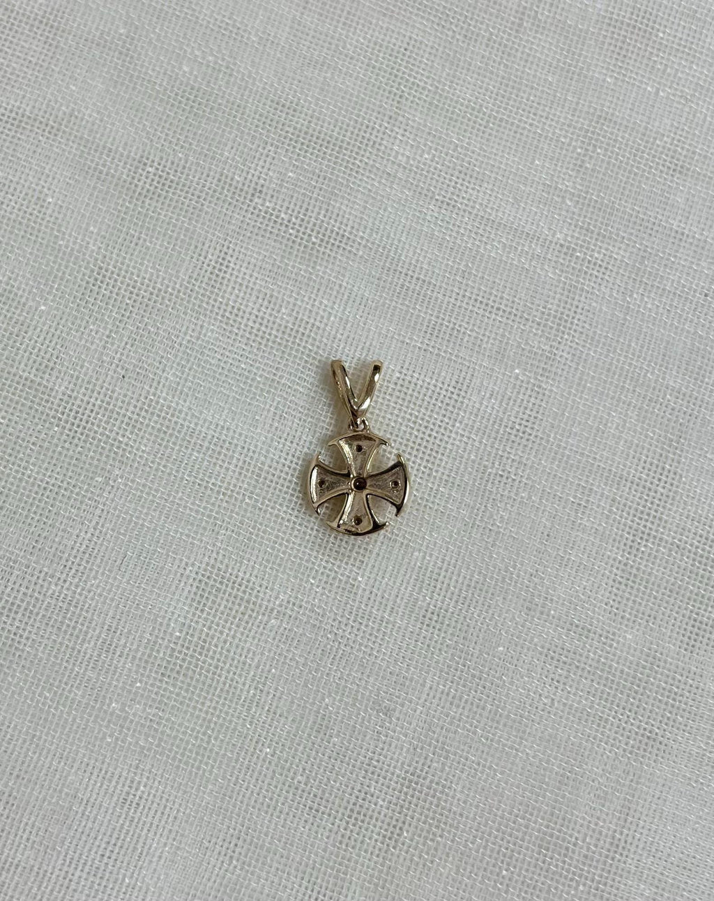 back view of gold cross pendant, sitting on beige fabric background 