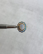 Gold ring with opal stones held by silver tool above a white background