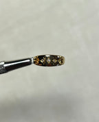 A close-up of a small gold ring held by metal tweezers against a soft white background.