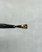 side view of gold ring with engraved swirl pattern, held by silver metal tool above soft white background 