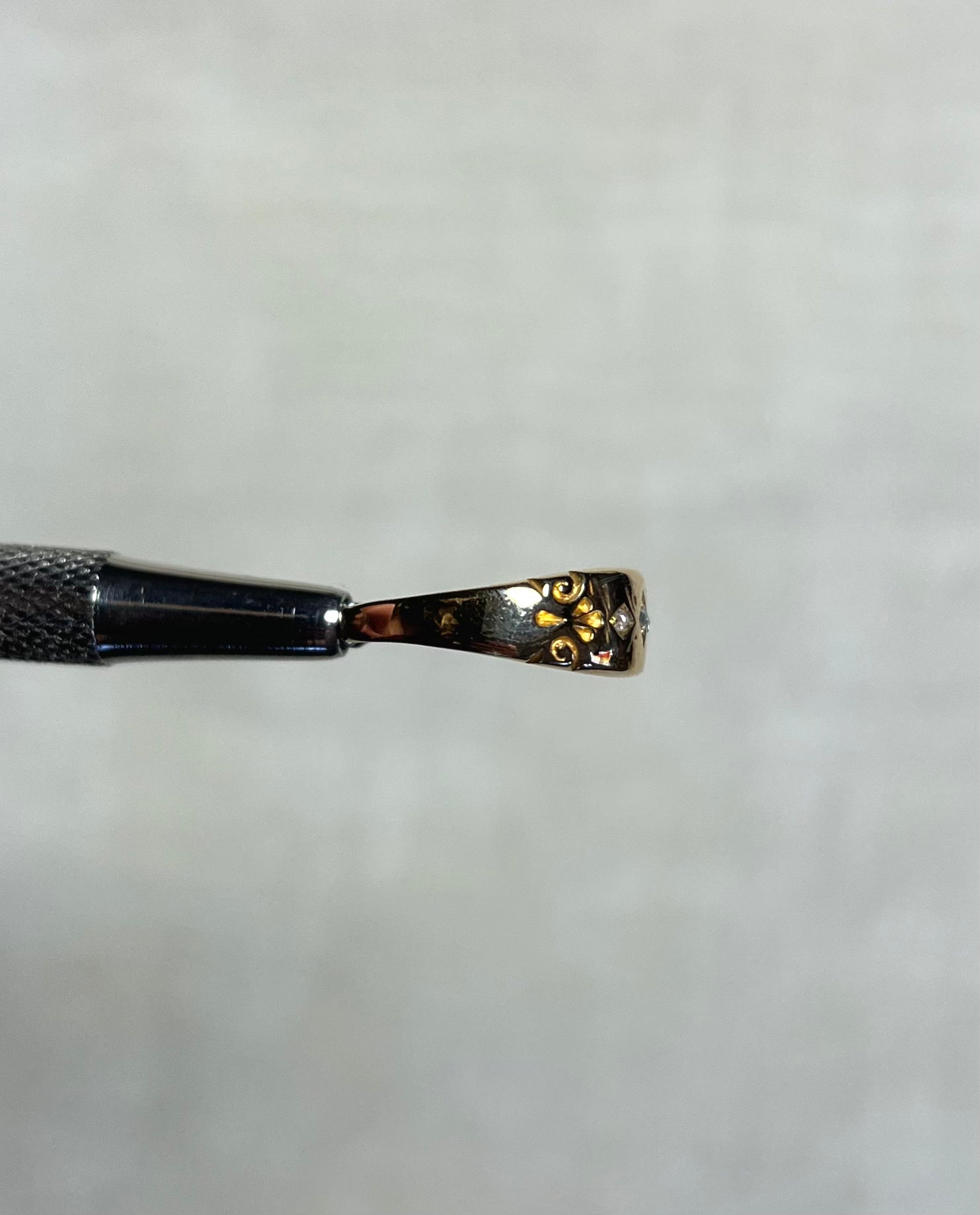 side view of gold ring with engraved swirl pattern, held by silver metal tool above soft white background 