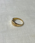 a vintage gold ring with diamonds. and swirl patten shoulders, resting on white fabric background 