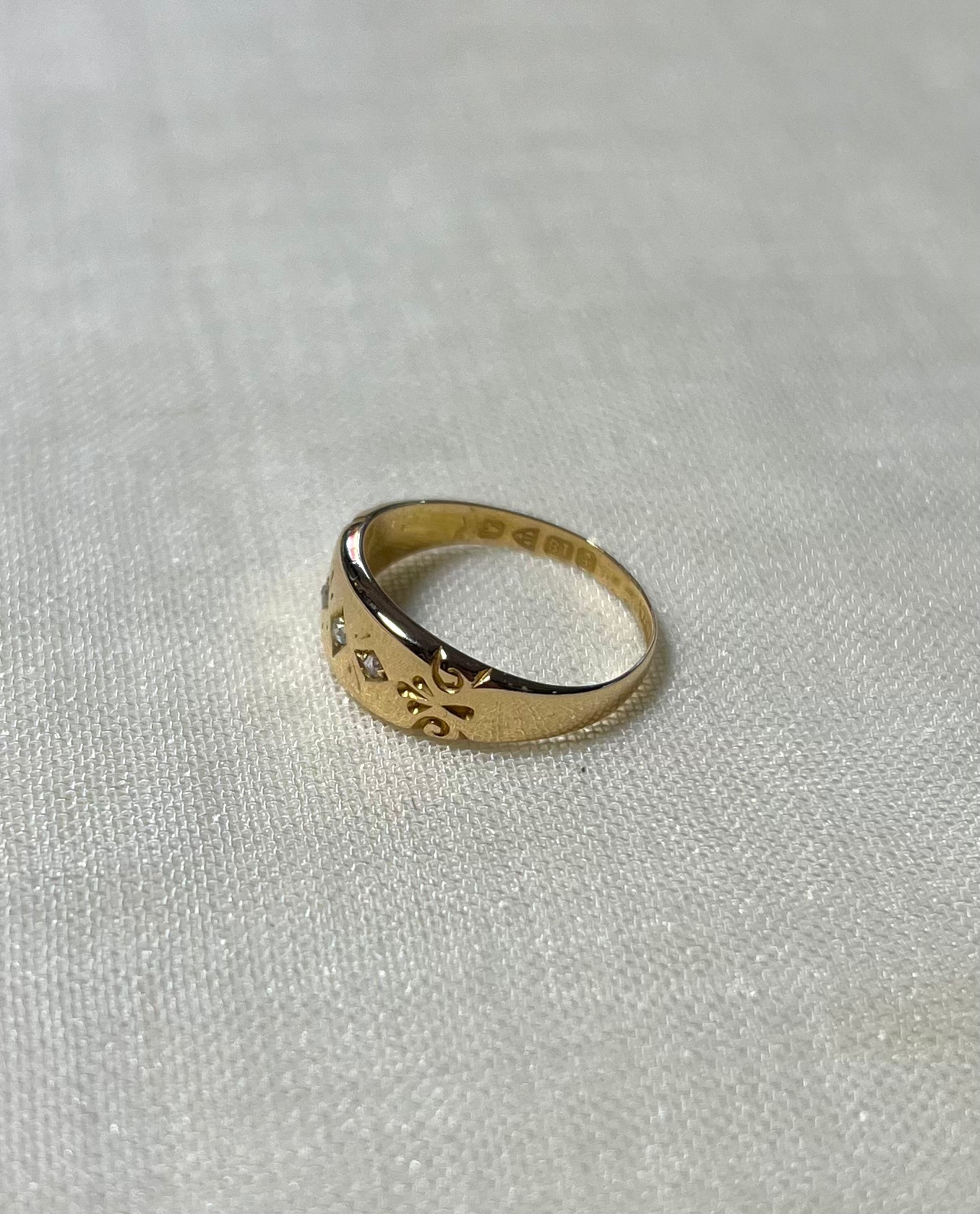 a vintage gold ring with diamonds. and swirl patten shoulders, resting on white fabric background 