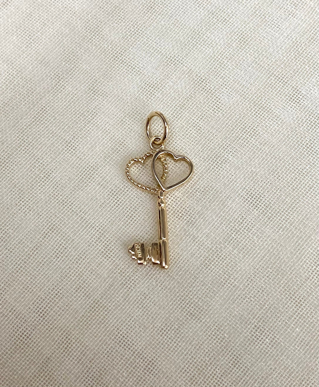 Gold key-shaped pendant with heart designs on a light fabric background