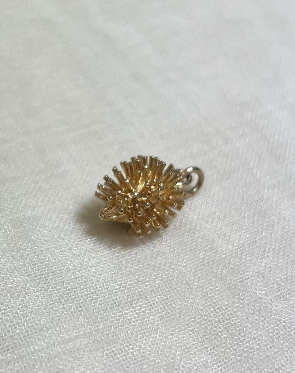 gold hedgehog charm resting on cream fabric background 