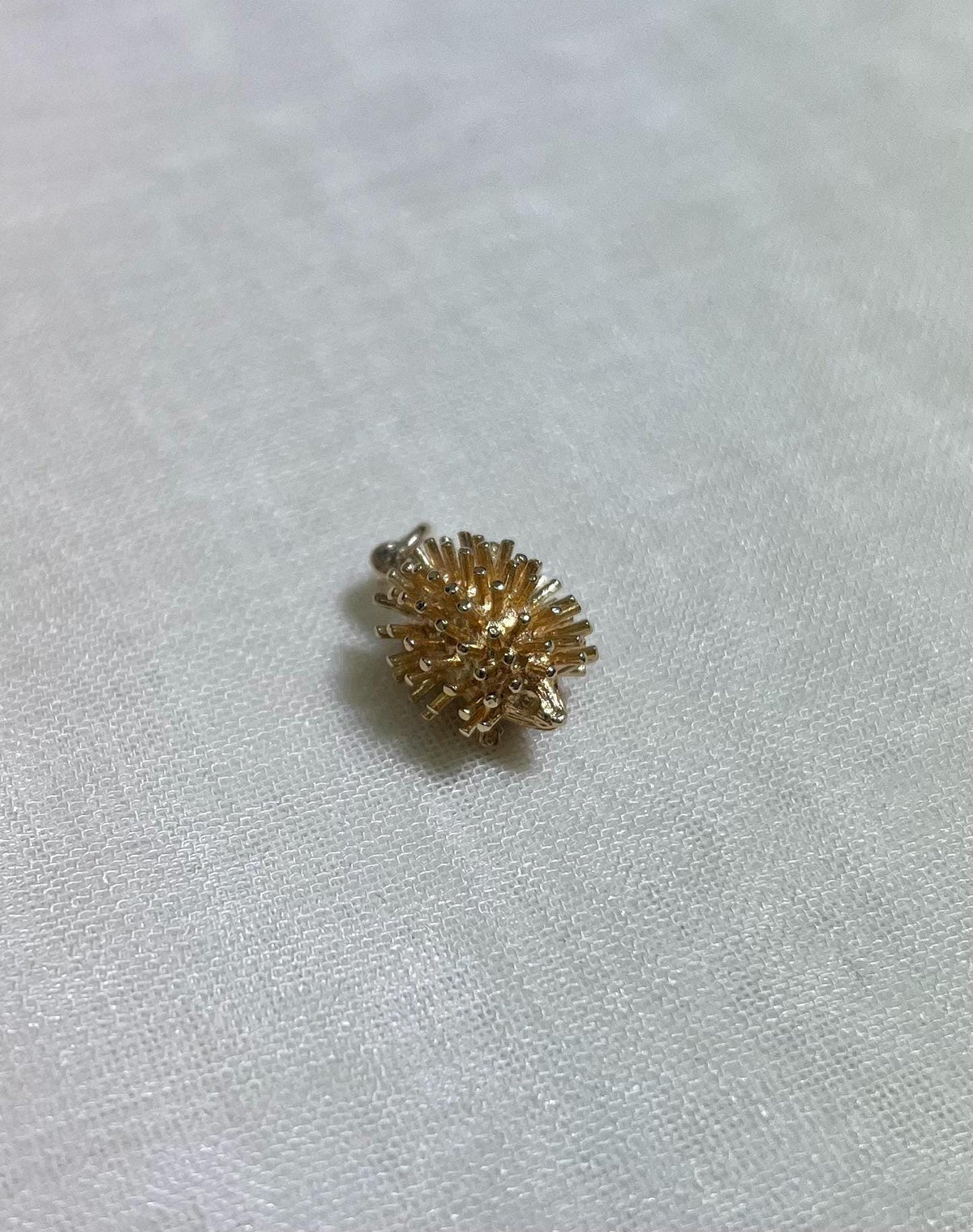 gold hedgehog charm on cream fabric background 