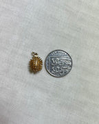gold hedgehog charm next to ten pence coin on cream fabric background
